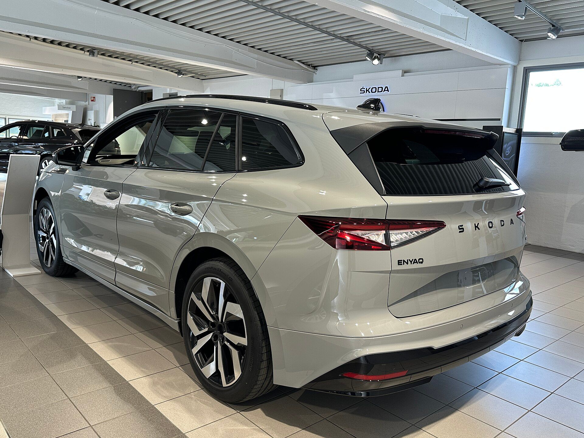 Škoda Enyaq Sportline (2025 facelift) gümüş, showroom'da arkadan üç çeyrek görünüm
