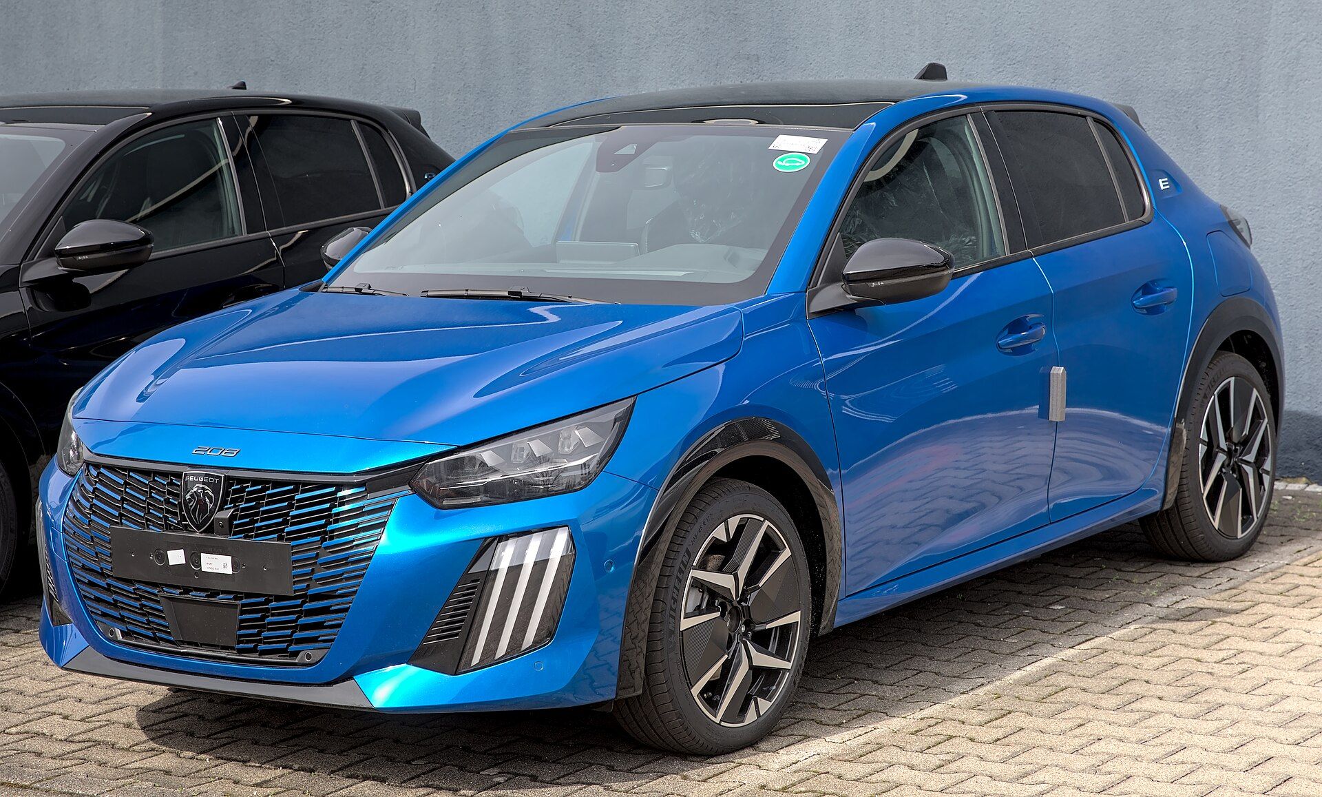 Mavi Peugeot E-208 (2023 makyajlı), ön çapraz görünüm ve üç pençeli gündüz farı imzası